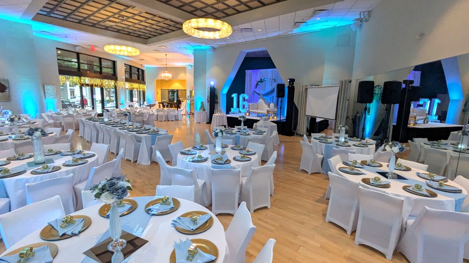 Midtown Ballroom set for a Sweet 16 celebration with round dining tables, chandeliers, blue event lighting and a stage